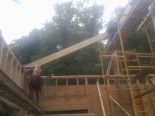 Carpenter raising a rafter beam on a new second story frame in Hartland