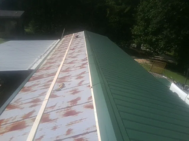 Old rusted panels beside newly installed green metal roofing — Wind Damage Roof Repair by Roofing Brothers in Hartland