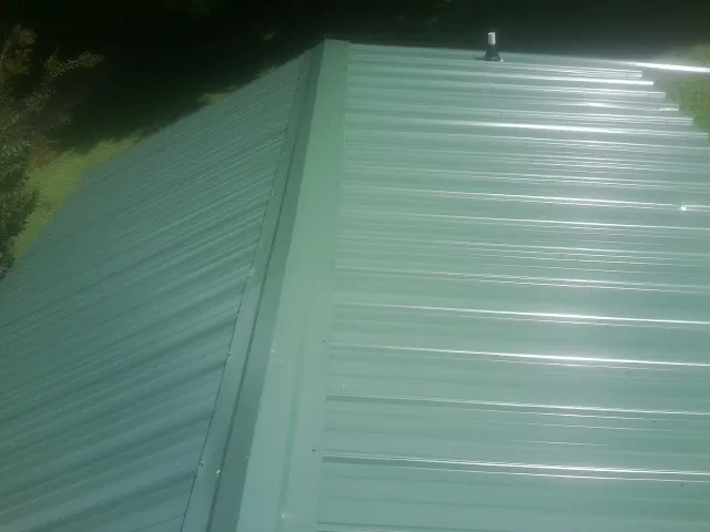 New green metal panels meeting at the ridge of a roof — Flat Roof Repair work by our crew in Hartland